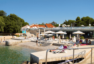Solrige liggestole og parasoller på stranden ved Camping Porto Sole i Istrien, Kroatien, med folk, der slapper af.