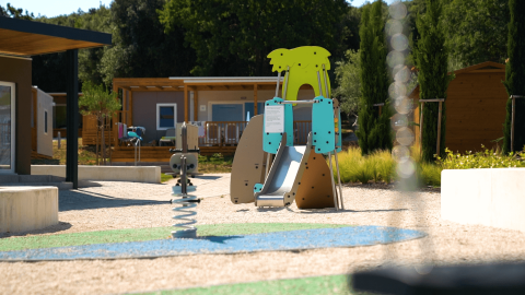 Parque infantil con tobogán y balancín frente a cabañas en Camping Porto Sole, Istria, Croacia, soleado día.