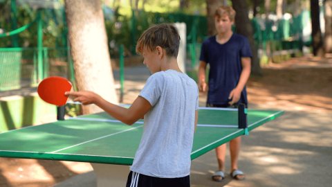 Dos chicos juegan al tenis de mesa al aire libre en Camping Porto Sole, un parque vacacional en Istria, Croacia.