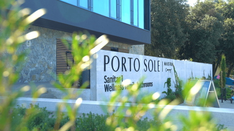 Cartello d'ingresso al Camping Porto Sole, parco vacanze in Istria, Croazia, con piante e edificio moderno.