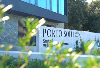 Cartello d'ingresso al Camping Porto Sole, parco vacanze in Istria, Croazia, con piante e edificio moderno.
