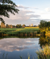 Vista idílica de un lago, campos verdes y edificio al fondo en el parque Hoeve Zeeland en los Países Bajos.