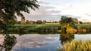 Vista idílica de un lago, campos verdes y edificio al fondo en el parque Hoeve Zeeland en los Países Bajos.