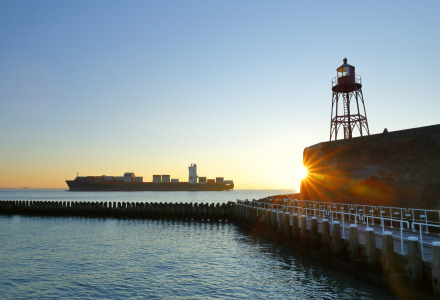 Atardecer en el puerto de Veere, Zelanda, con un faro y un buque portacontenedores al fondo.