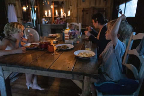 Een familie geniet van een gezellig diner bij kaarslicht in een houten chalet op Feather Down Figari Corsica, Frankrijk.