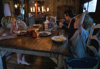 Een familie geniet van een gezellig diner bij kaarslicht in een houten chalet op Feather Down Figari Corsica, Frankrijk.