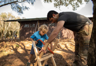 A man helps a boy saw wood outdoors at Feather Down Figari Corsica holiday park in Corsica, France.