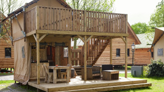 Buitenbeeld van een luxe Forest Lodge Junior safaritent met houten terras bij Sandberghe in Nederland