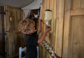 Een kind gebruikt een wandgemonteerde koffiemolen in een houten hut op Feather Down Figari Corsica vakantiedomein.
