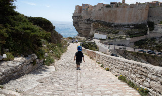 Un niño camina por un sendero empedrado cerca de Figari, Córcega, con vistas al mar y acantilados altos.