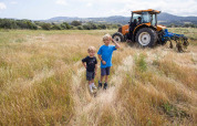 To drenge står på en mark nær Figari, Korsika, med en traktor og bjerge i baggrunden, Frankrig.
