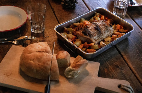 Cena rústica con pan, carne asada y verduras en mesa de madera en Feather Down Figari Corsica.