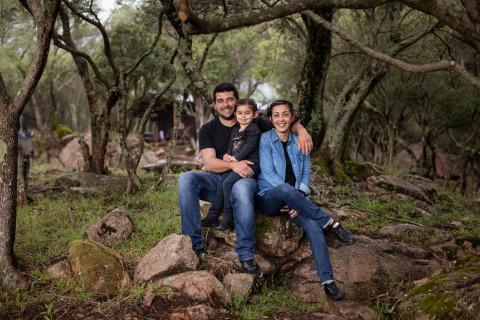 En familie sidder og smiler sammen på sten i en skov ved Feather Down Figari Corsica, Frankrig.