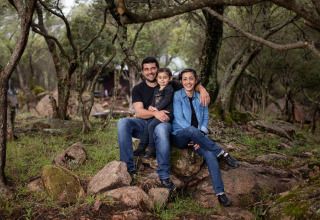 Een gezin zit samen glimlachend op stenen in het bos bij Feather Down Figari Corsica, Frankrijk.