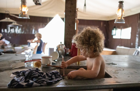 Bambino riccioluto gioca nel lavello della cucina in una tenda al Feather Down Figari Corsica holiday park.
