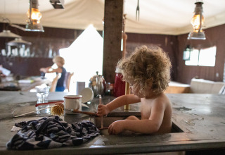 Bambino riccioluto gioca nel lavello della cucina in una tenda al Feather Down Figari Corsica holiday park.