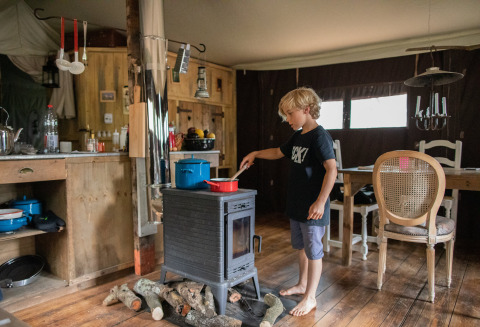 Boy cooking on a wood stove inside a cozy cabin at Feather Down Figari Corsica holiday park in France.
