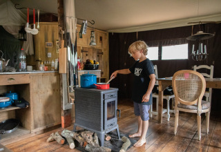 Boy cooking on a wood stove inside a cozy cabin at Feather Down Figari Corsica holiday park in France.