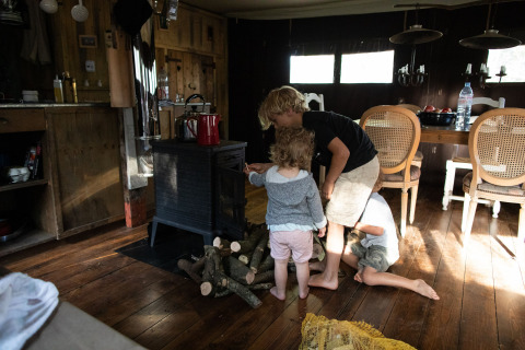 Children playing by a wood stove inside a cozy cabin at Feather Down Figari Corsica holiday park, France.