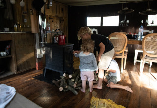 Kinderen spelen bij een houtkachel in een knusse hut op Feather Down Figari Corsica vakantiepark, Frankrijk.