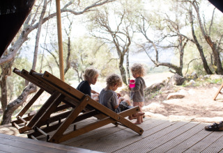 Family relaxing on a deck at Feather Down Figari Corsica holiday park, surrounded by woodland in France.