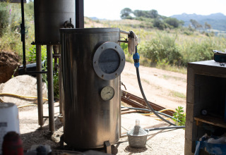 Grote metalen tank met manometer en slang buiten in het zonlicht bij Feather Down Figari Corsica vakantiepark, Frankrijk.