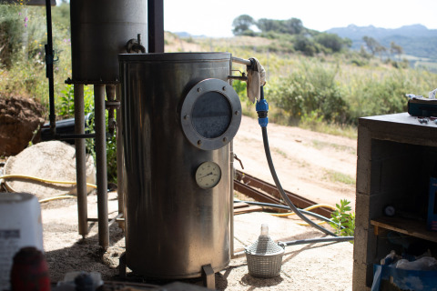 Grote metalen tank met manometer en slang buiten in het zonlicht bij Feather Down Figari Corsica vakantiepark, Frankrijk.