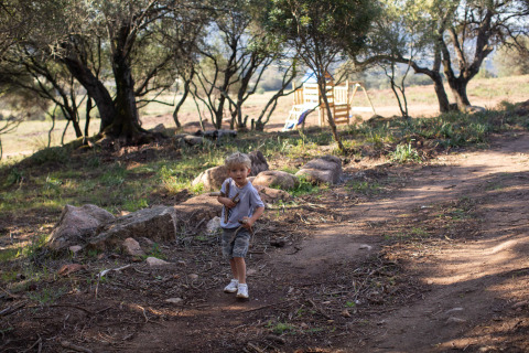 Un niño juega en una zona boscosa con un parque infantil al fondo en Feather Down Figari Corsica, Francia.