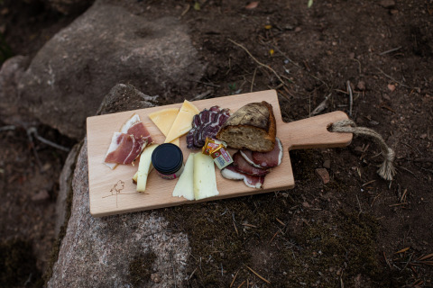 Houten plank met kaas, brood, charcuterie en confituur buiten bij Feather Down Figari Corsica, Frankrijk.
