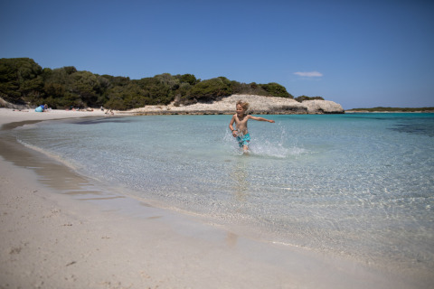 Ein Kind rennt durch das klare, flache Wasser an einem Sandstrand bei Figari auf Korsika, Frankreich.