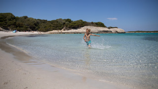 Un niño corre por aguas poco profundas y cristalinas en una playa de arena cerca de Figari, Córcega, Francia.