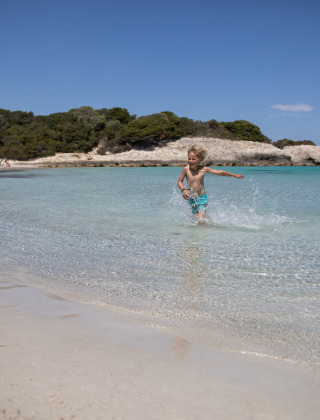 Un niño corre por aguas poco profundas y cristalinas en una playa de arena cerca de Figari, Córcega, Francia.