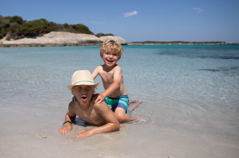 To glade børn leger i lavt vand på stranden ved Feather Down Figari Corsica feriepark i Frankrig.