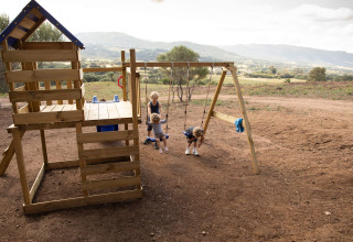 Kinderen spelen op een houten speeltoestel met schommels bij Feather Down Figari Corsica vakantiepark.