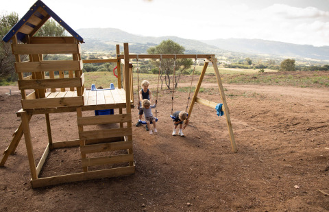 Kinder spielen auf einem Holzspielplatz mit Schaukeln im Feather Down Figari Corsica Ferienpark.