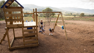 Niños juegan en un parque infantil de madera con columpios en Feather Down Figari Corsica, Francia.