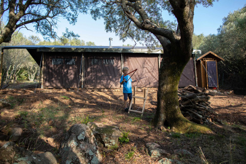 Kind speelt met boog en pijl voor safaritent op Feather Down Figari Corsica vakantiepark, Corsica, Frankrijk.