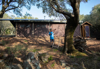 Niño juega con arco y flecha frente a tienda de safari en Feather Down Figari Corsica, parque vacacional en Córcega.