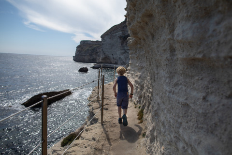 Ein Junge spaziert auf einem schmalen Klippenpfad an der Küste bei Figari, Korsika, Frankreich entlang.
