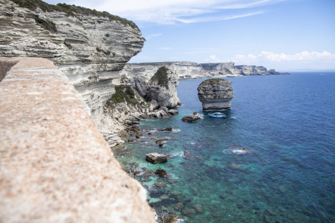 Acantilados de piedra caliza y mar turquesa cerca de Figari, Córcega, con un destacado islote marino.