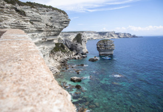 Acantilados de piedra caliza y mar turquesa cerca de Figari, Córcega, con un destacado islote marino.