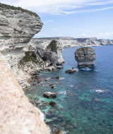 Acantilados de piedra caliza y mar turquesa cerca de Figari, Córcega, con un destacado islote marino.