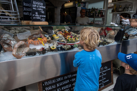 Two children look at a display of fresh seafood in a glass case at a market stall in Corsica, France.