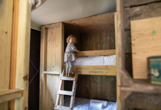 Un jeune enfant grimpe une échelle en bois vers un lit superposé dans une cabane rustique à Feather Down Figari Corse.