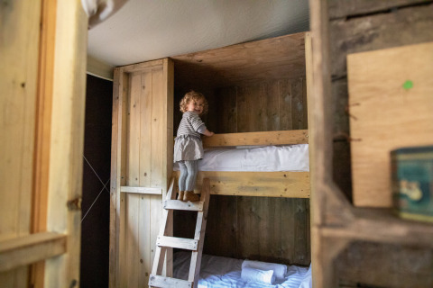 Un jeune enfant grimpe une échelle en bois vers un lit superposé dans une cabane rustique à Feather Down Figari Corse.