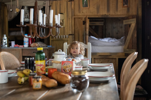 Un niño se sienta en la mesa del desayuno con pan y jugo en una cabaña de madera en Feather Down Figari Corsica, Francia.
