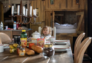 Ein Kind sitzt am Frühstückstisch mit frischem Brot und Saft in einer Holzhütte bei Feather Down Figari Corsica, Frankreich.