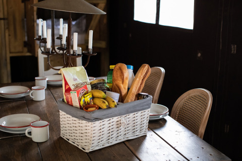 Cesta de desayuno con baguettes y frutas sobre una mesa de madera en una casa vacacional en Córcega, Francia.