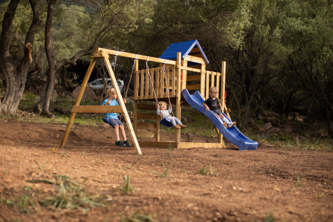 Niños jugando en un parque de madera con tobogán y columpios en Feather Down Figari Córcega, Francia.