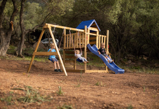 Kinder spielen auf einem Holzspielplatz mit Rutsche und Schaukeln im Feather Down Figari Korsika Park.
